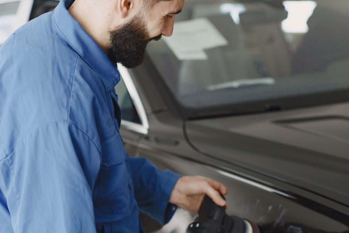 Hands working a polishing tool across a car body panel