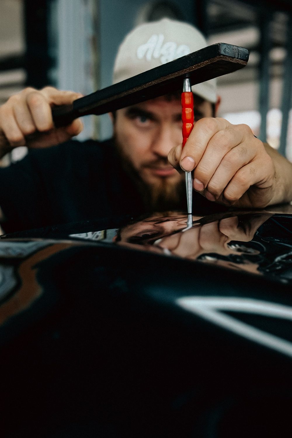 Technician working a dent out of a panel under workshop lights