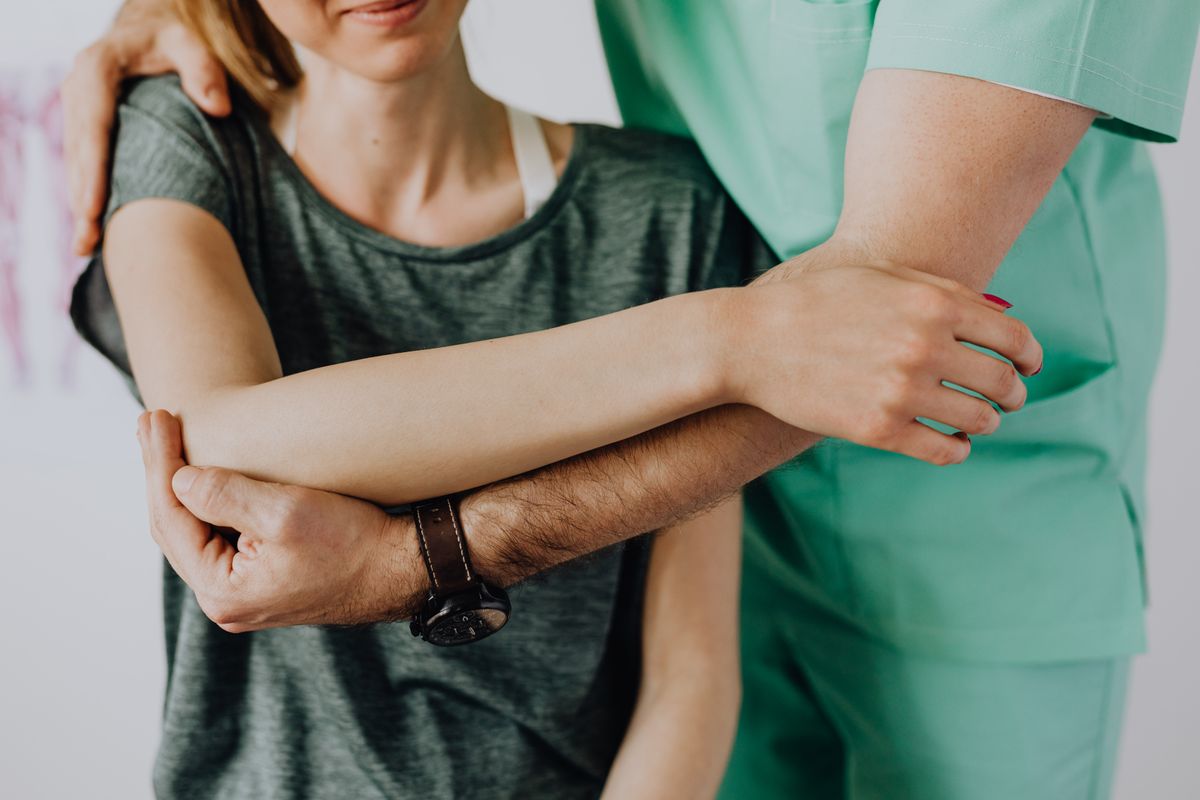Physiotherapist assessing a patient's shoulder in a treatment room