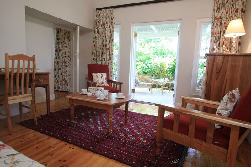 A suite sitting room with a red armchair and table, patio doors standing open