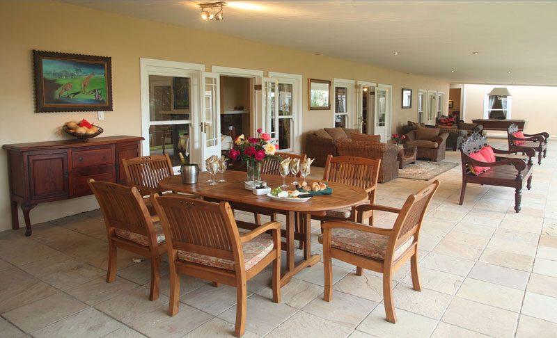 A covered patio table set with a wine cooler, flowers and canapés