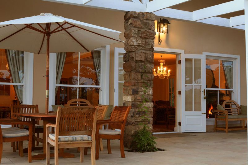 A pergola table beside a stone pillar, warm light through the French doors