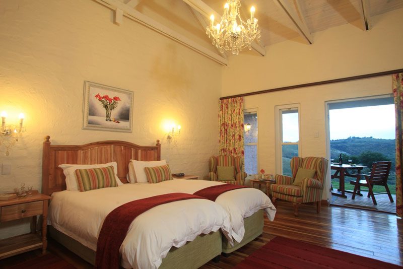A cottage bedroom with twin beds, striped wing chairs and a view down the valley