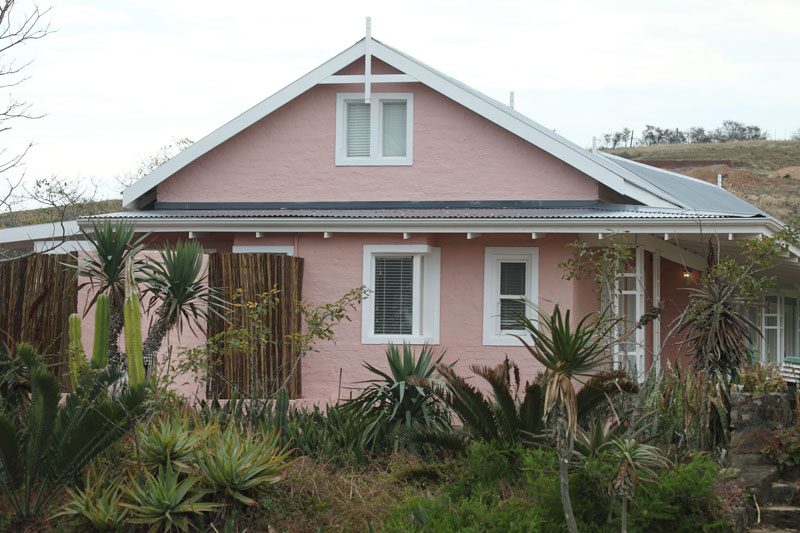 A pink gabled cottage behind a garden of aloes and succulents