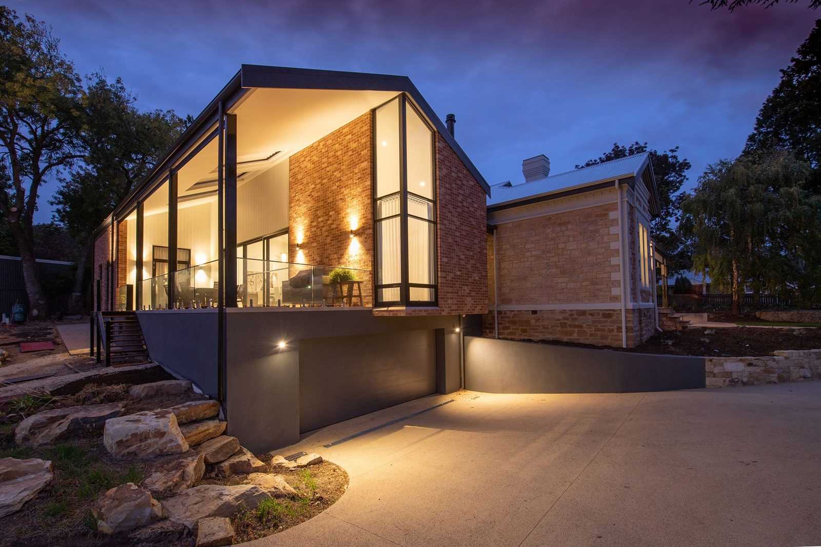 A modern home lit up at dusk behind its boundary wall
