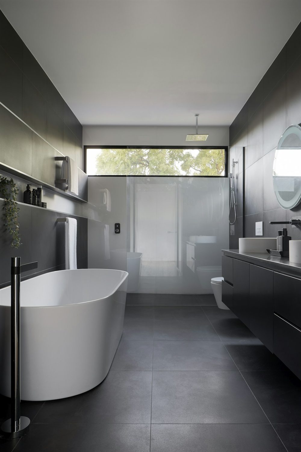 Dark tiled bathroom with a freestanding bath and floor-standing mixer