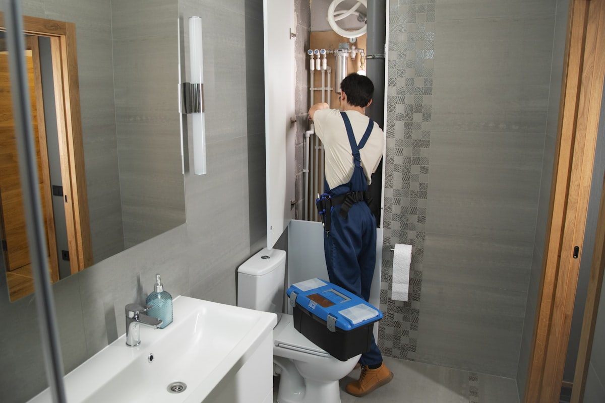 Plumber fitting pipework in a tiled bathroom